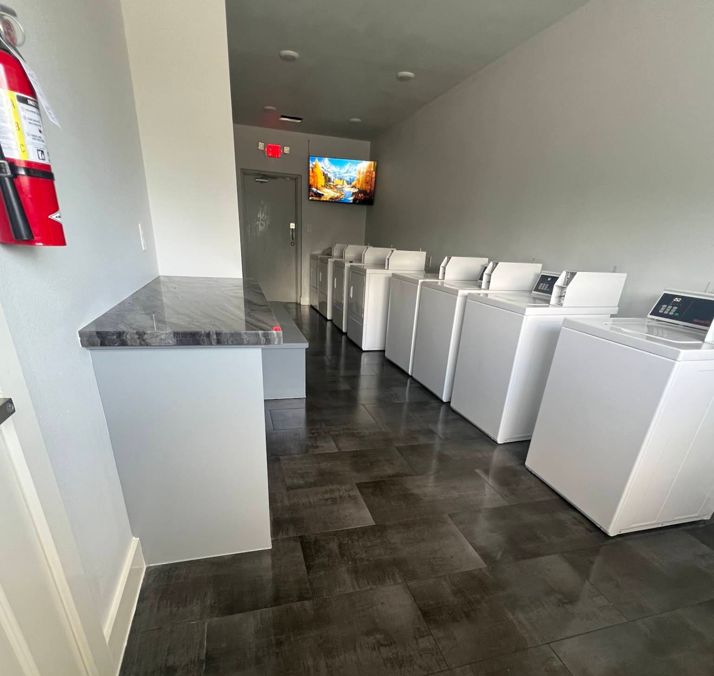 Clean laundry room with a row of machines and folding counters